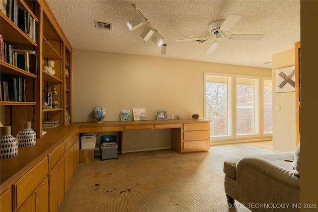 office space featuring built in desk, light colored carpet, visible vents, ceiling fan, and a textured ceiling