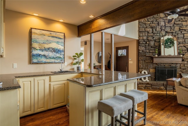 kitchen with a peninsula, a sink, open floor plan, dark stone counters, and a kitchen bar