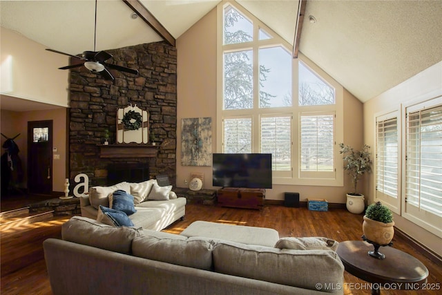 living area featuring baseboards, ceiling fan, wood finished floors, a stone fireplace, and high vaulted ceiling