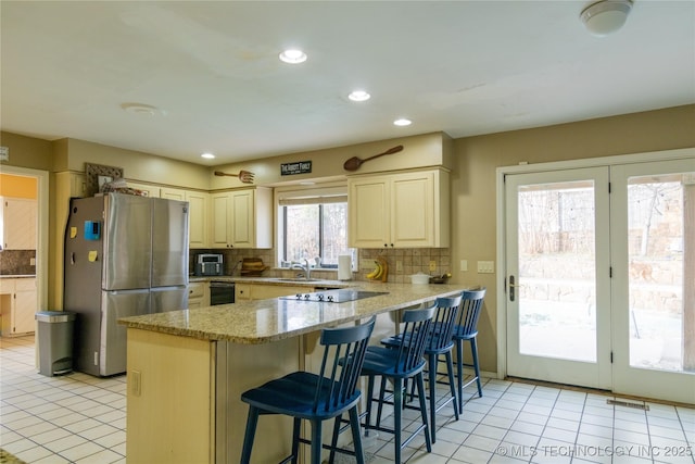 kitchen with a breakfast bar area, a peninsula, backsplash, light stone countertops, and black appliances