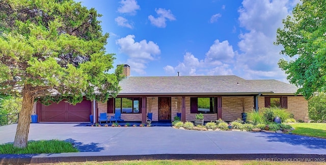 ranch-style home with a chimney, a porch, an attached garage, stone siding, and driveway