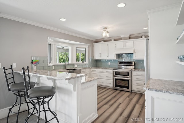 kitchen with range with two ovens, white cabinets, a sink, a peninsula, and a kitchen bar