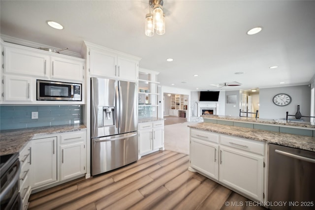 kitchen featuring a lit fireplace, stainless steel appliances, backsplash, and white cabinets