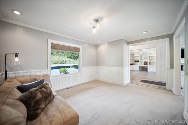 sitting room with a wainscoted wall, built in shelves, ornamental molding, and light colored carpet