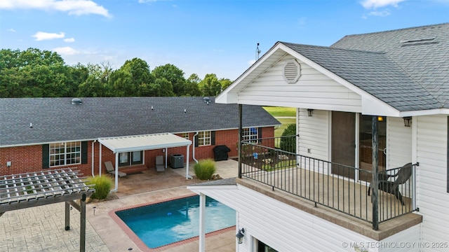 rear view of property featuring a balcony, brick siding, roof with shingles, an outdoor pool, and a patio area