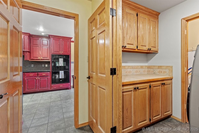 kitchen featuring dark countertops, dobule oven black, tile patterned flooring, and backsplash