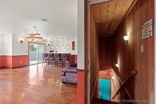 hallway with wood walls, wooden ceiling, wood finished floors, and visible vents