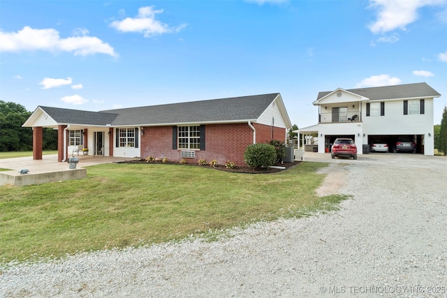 view of front of house with central AC unit, gravel driveway, a front lawn, a carport, and brick siding