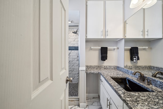 full bath featuring marble finish floor, a tile shower, and vanity