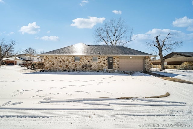 snow covered property with a garage and stone siding