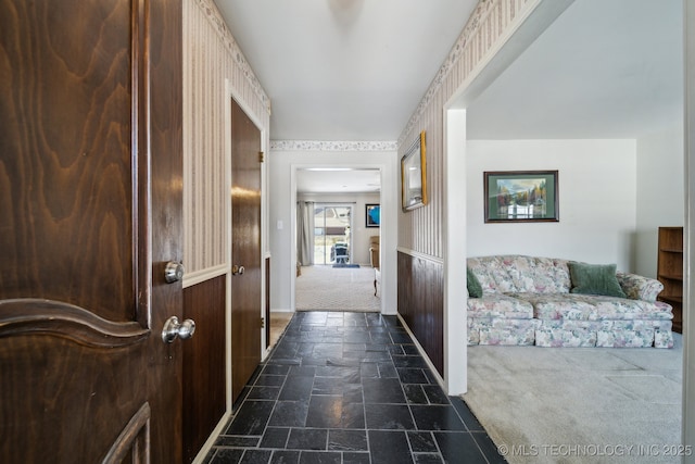 hall with stone tile floors and dark carpet