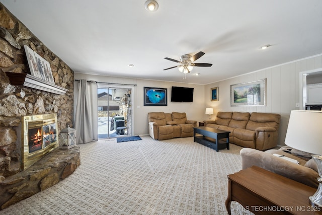 living room with ceiling fan, ornamental molding, carpet flooring, and a stone fireplace