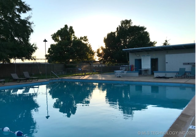 pool at dusk with fence, a community pool, and a patio