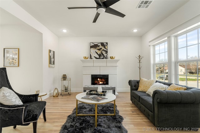 living area with recessed lighting, visible vents, light wood-style flooring, a glass covered fireplace, and baseboards