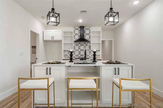 kitchen featuring open shelves, light countertops, hanging light fixtures, white cabinetry, and wall chimney range hood