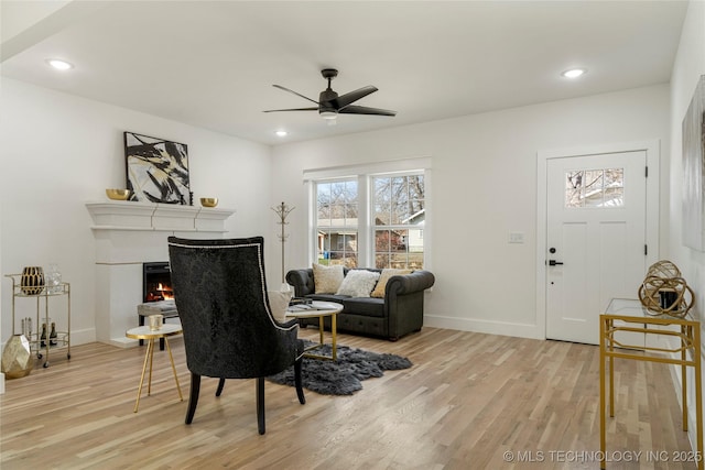 sitting room with light wood-style floors, a lit fireplace, and baseboards