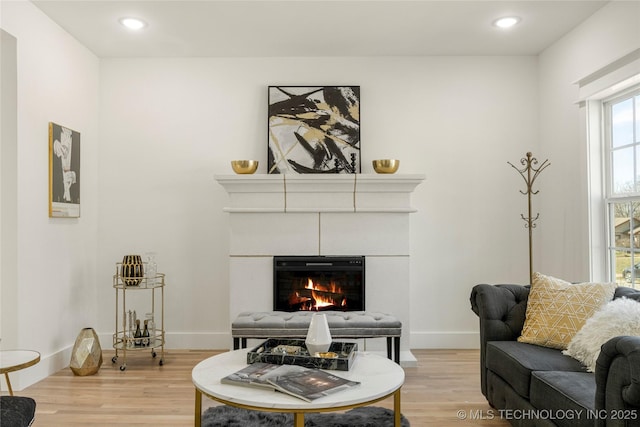 living area featuring recessed lighting, a glass covered fireplace, light wood-style flooring, and baseboards