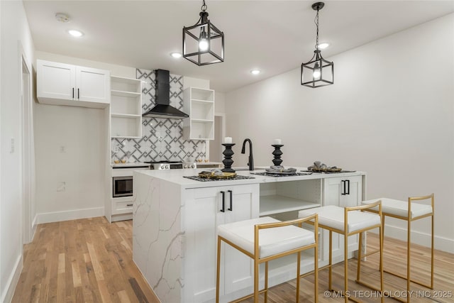 kitchen featuring open shelves, wall chimney range hood, white cabinetry, and pendant lighting