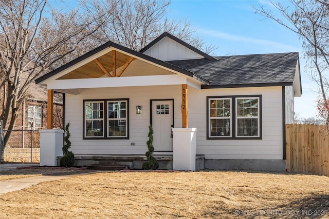 bungalow-style house featuring covered porch, fence, board and batten siding, and roof with shingles