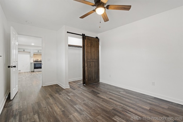 spare room featuring dark wood-style floors, a barn door, baseboards, and ceiling fan