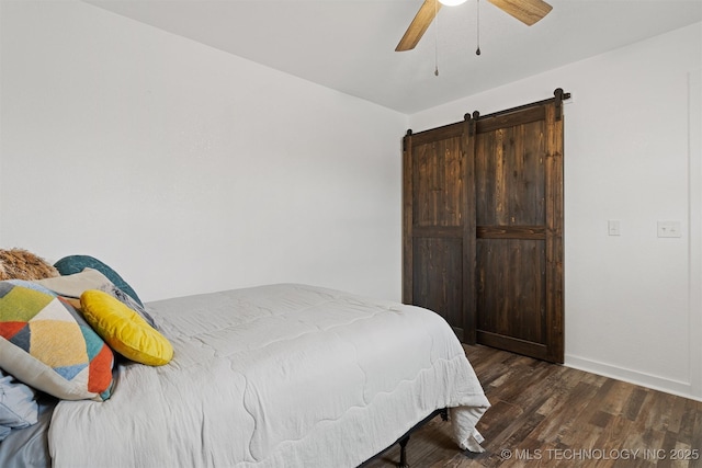 bedroom with a ceiling fan, a barn door, baseboards, and wood finished floors