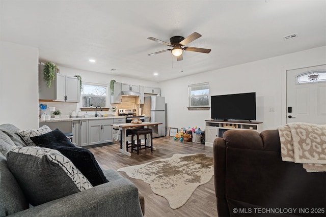 living area with recessed lighting, visible vents, ceiling fan, and wood finished floors