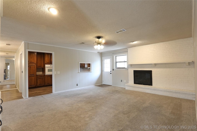 unfurnished living room featuring a brick fireplace, a textured ceiling, visible vents, and carpet flooring