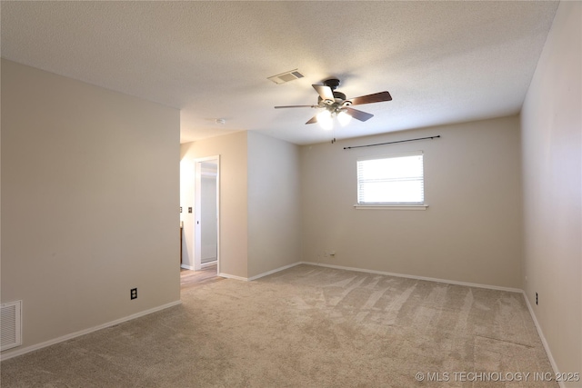 spare room featuring light colored carpet, visible vents, ceiling fan, a textured ceiling, and baseboards