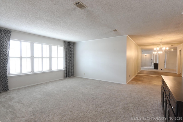 unfurnished room featuring visible vents, an inviting chandelier, light carpet, a textured ceiling, and baseboards