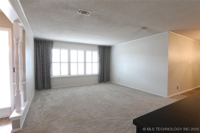 empty room with visible vents, ornamental molding, light carpet, a textured ceiling, and baseboards