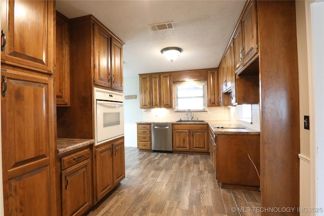 kitchen featuring brown cabinets, oven, dishwasher, and a sink