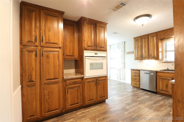 kitchen featuring light wood-style flooring, visible vents, white oven, light stone countertops, and dishwasher