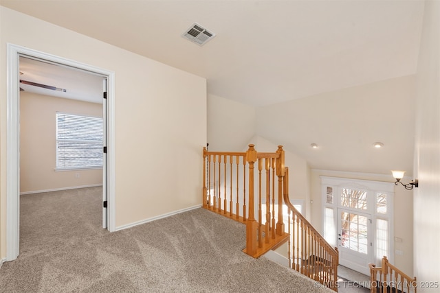 hallway featuring visible vents, light colored carpet, a wealth of natural light, and an upstairs landing