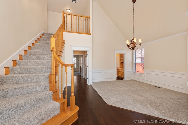 stairs featuring a notable chandelier, visible vents, wainscoting, wood finished floors, and high vaulted ceiling