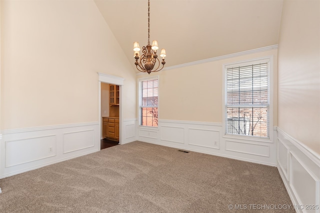 carpeted spare room with lofted ceiling, a wainscoted wall, visible vents, and a notable chandelier