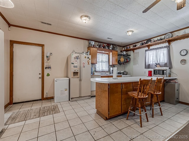 kitchen with white refrigerator with ice dispenser, brown cabinetry, stainless steel microwave, a peninsula, and light countertops