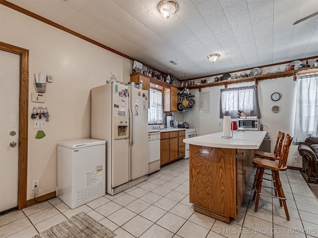 kitchen with white appliances, a kitchen breakfast bar, light countertops, brown cabinetry, and crown molding