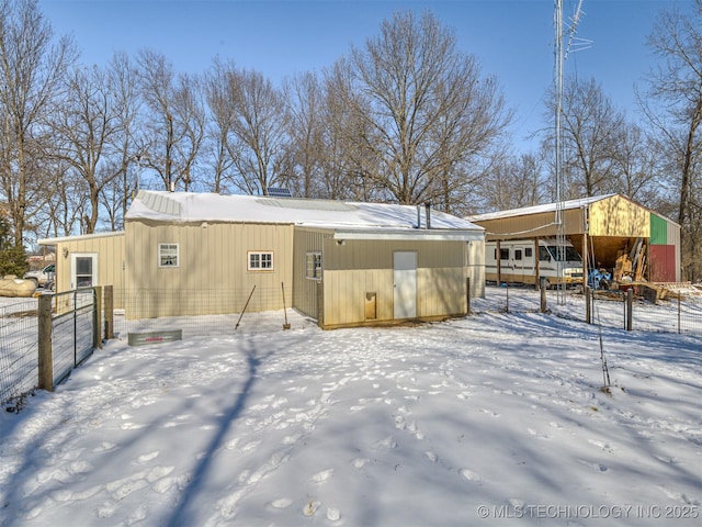 snow covered structure with an outbuilding and fence