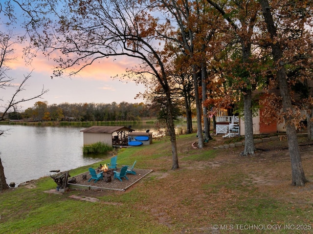 yard at dusk featuring an outdoor fire pit and a water view