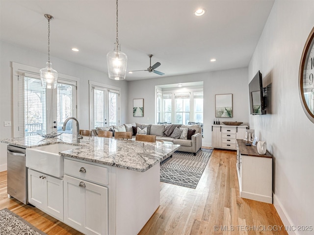 kitchen with stainless steel dishwasher, open floor plan, white cabinets, a sink, and an island with sink