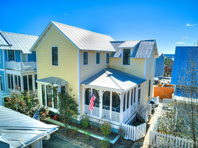 view of front of property featuring a sunroom, fence, metal roof, and a standing seam roof