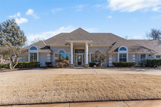 view of front of house with a shingled roof, a front yard, and stucco siding