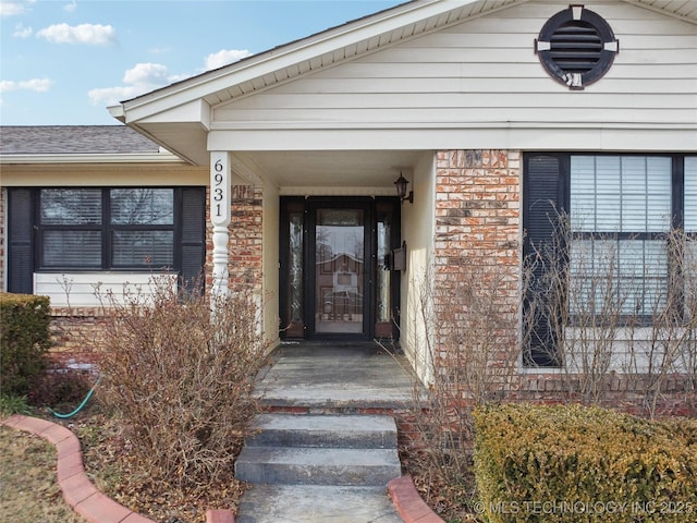 doorway to property with brick siding and roof with shingles