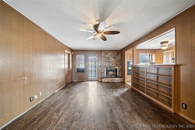 unfurnished living room with visible vents, ceiling fan, dark wood-style flooring, wood walls, and a fireplace