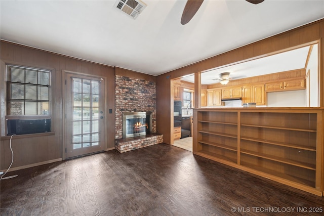 unfurnished living room featuring a brick fireplace, a healthy amount of sunlight, visible vents, and wood finished floors