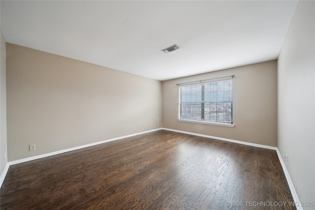 empty room featuring dark wood-style floors, visible vents, and baseboards