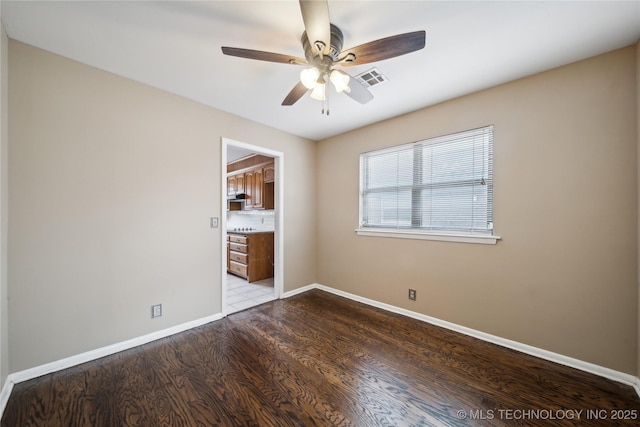 unfurnished room with a ceiling fan, visible vents, baseboards, and wood finished floors