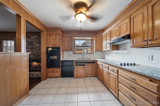 kitchen with under cabinet range hood, visible vents, light stone countertops, black appliances, and brown cabinetry