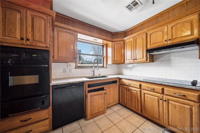 kitchen with light stone counters, brown cabinetry, a sink, under cabinet range hood, and black appliances