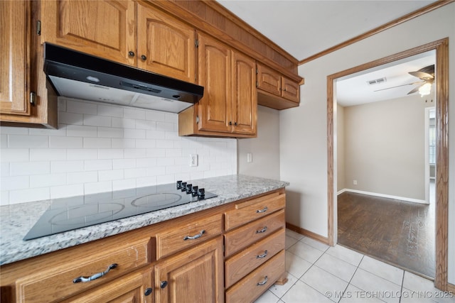 kitchen with visible vents, brown cabinetry, light stone countertops, black electric cooktop, and under cabinet range hood